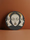 Circular ceramic coaster with a black, star-speckled background. Three white faces are depicted: a central face looking forward and two profiles on either side, all with closed eyes. A golden crescent moon arches over the central face. The coaster has a white rim indicating a cork backing and is 4.04 inches in diameter.